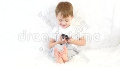 小男孩坐在白色沙发上，喜欢玩智能手机。